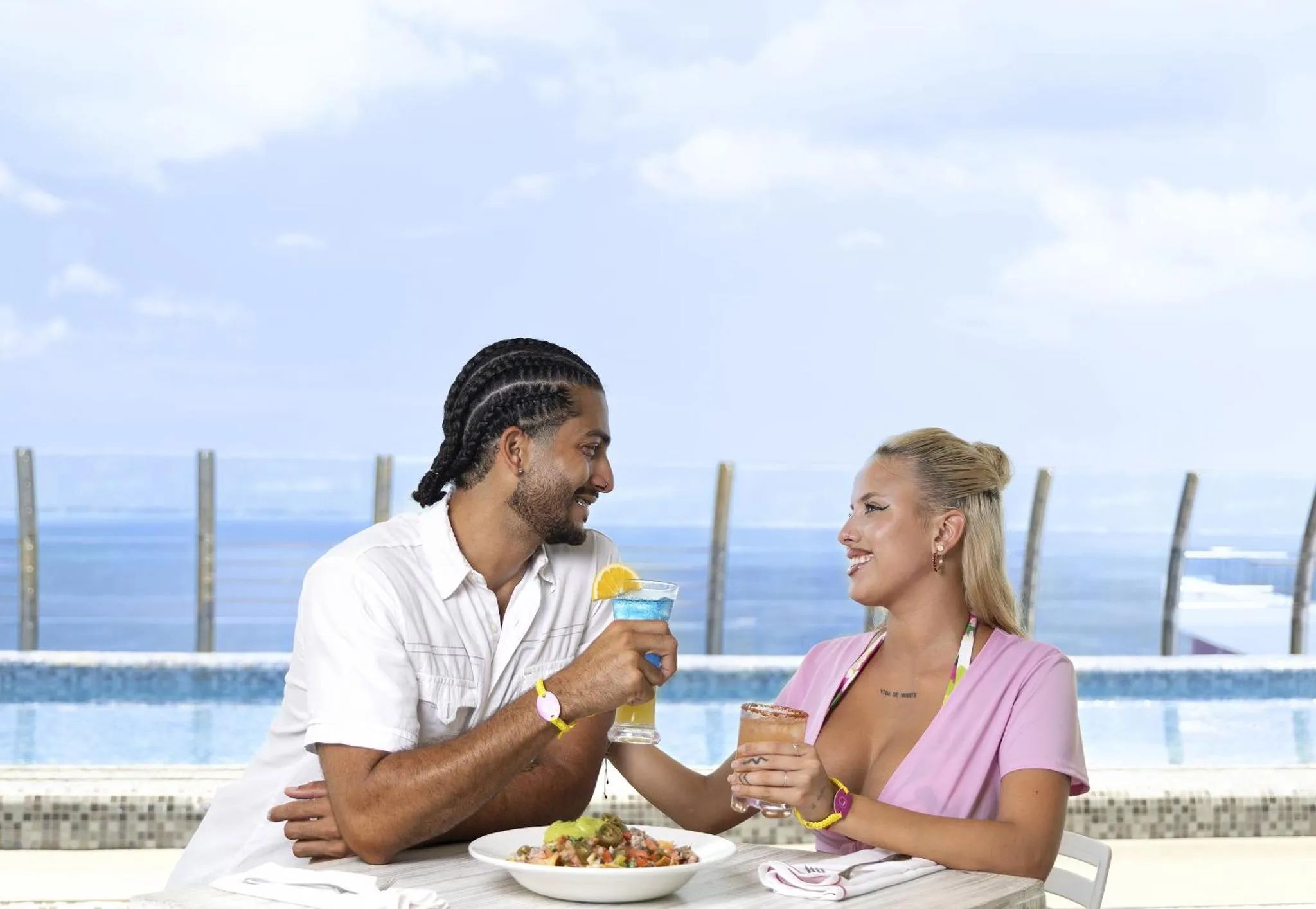 Un couple souriant partage un moment de détente avec des boissons et des plats sur une terrasse.