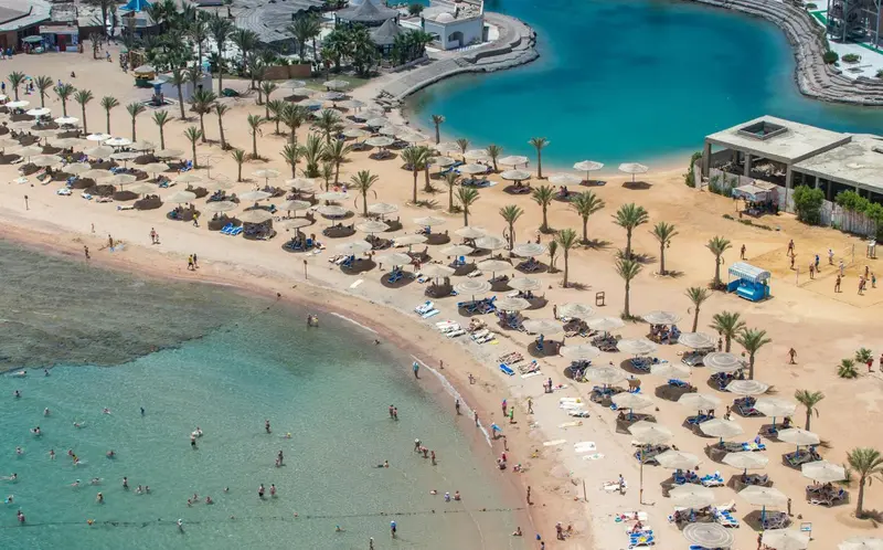 Vue aérienne d'une plage de sable fin bordée d'une eau turquoise et de parasols.