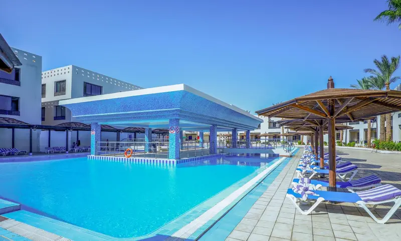 Piscine turquoise bordée de transats sous des parasols, avec un bar en fond.