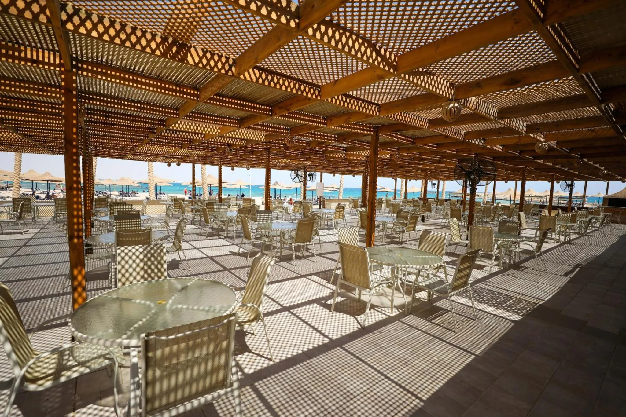 Terrasse ombragée avec tables et chaises en osier face à la mer.