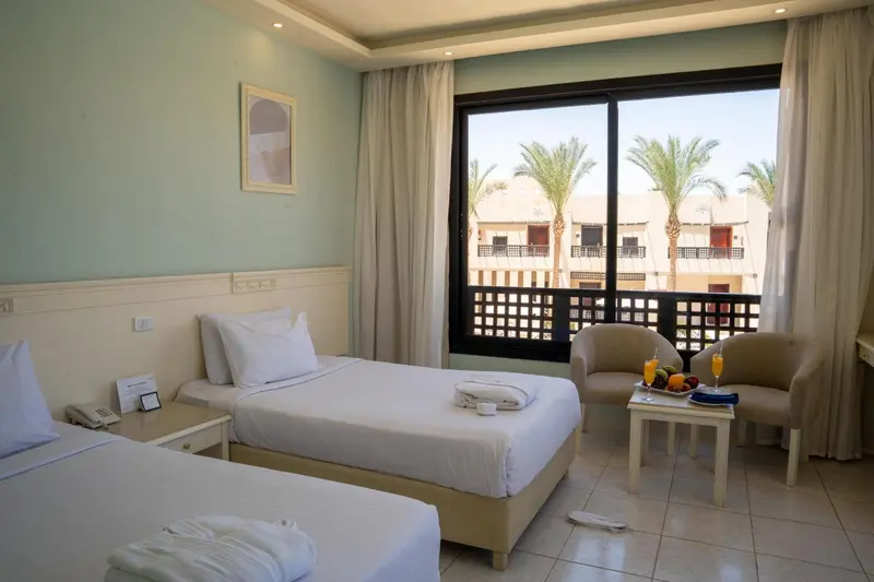 Chambre lumineuse avec lits simples et vue sur une végétation tropicale.
