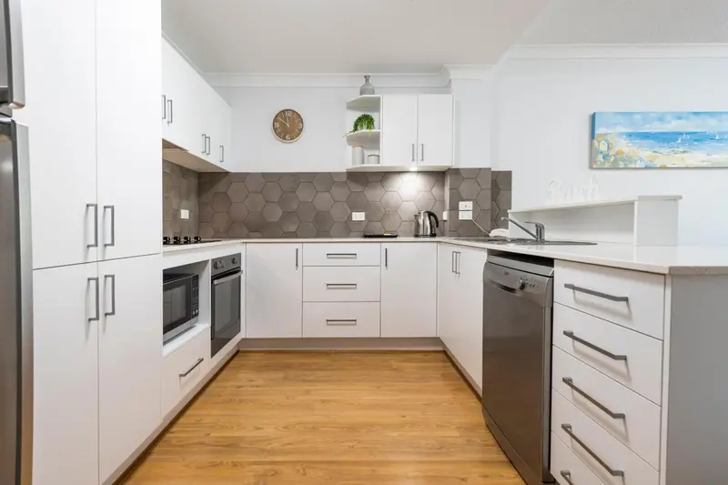 Cuisine moderne et lumineuse avec des armoires blanches et un plan de travail en bois.