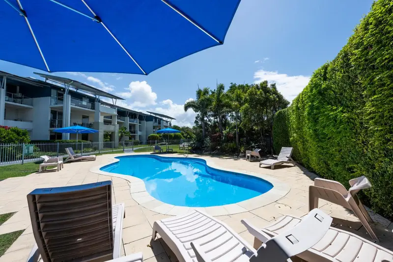 Transats et parasols bordent une piscine turquoise dans un jardin soigné.