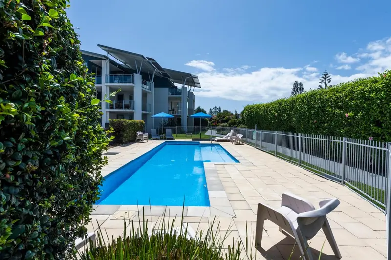 Une piscine rectangulaire bordée de chaises longues et de végétation luxuriante.