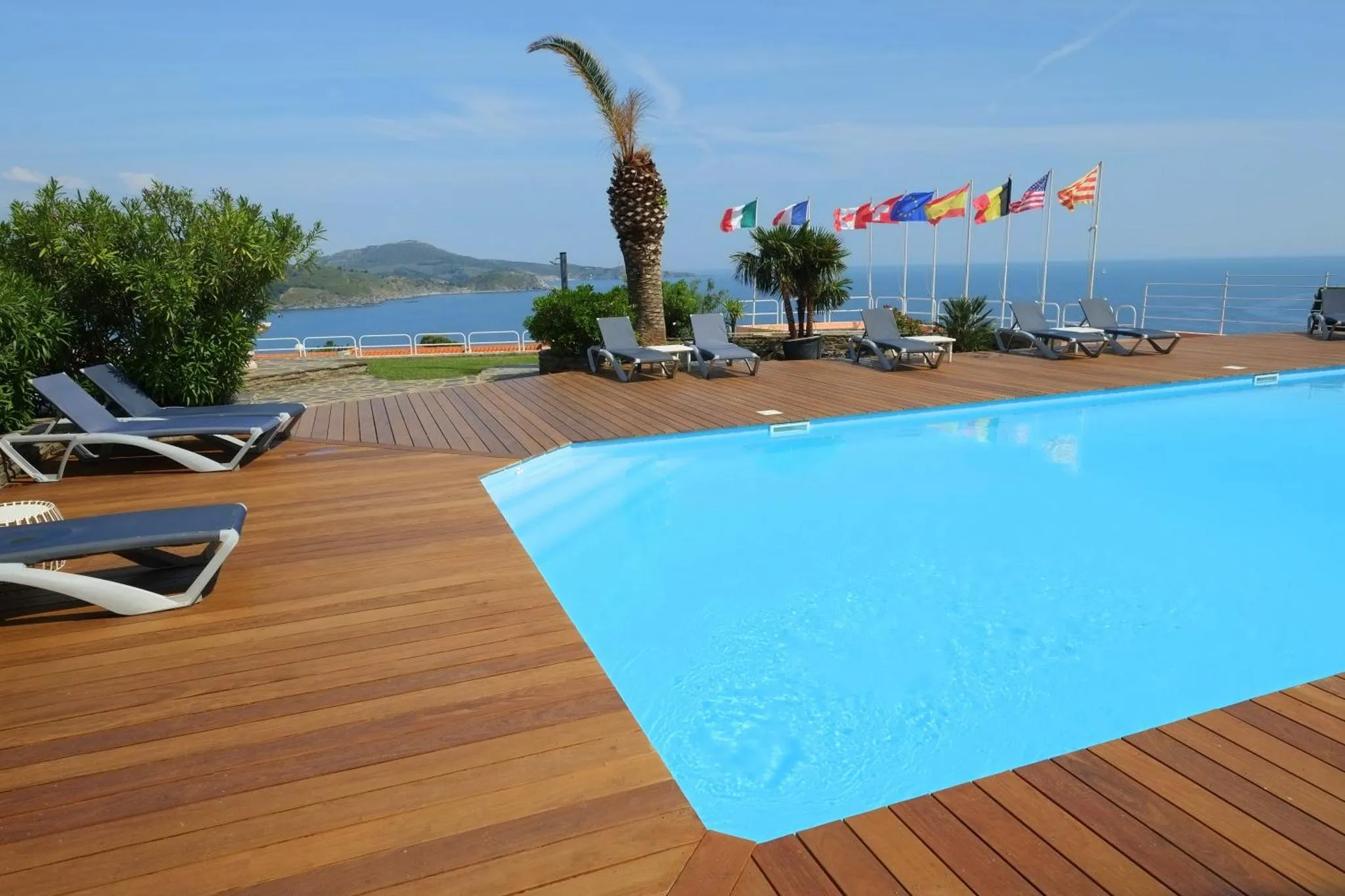 Terrasse en bois avec transats et piscine face à la mer.