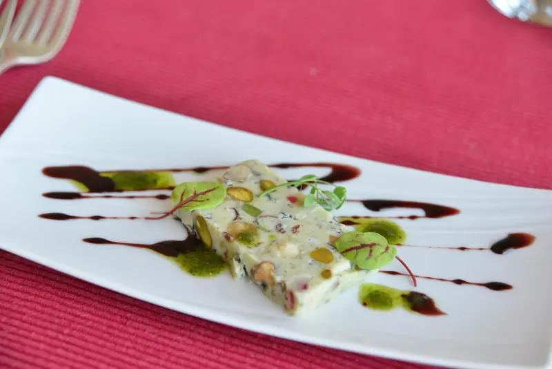 Assiette rectangulaire blanche présentant un dessert à base de crème, de fruits secs et d'une sauce foncée.