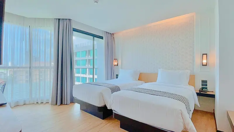 Chambre lumineuse avec deux lits simples et vue sur l'extérieur.