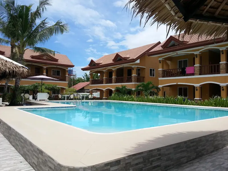 Bâtiment jaune à deux étages avec piscine au premier plan et végétation tropicale.