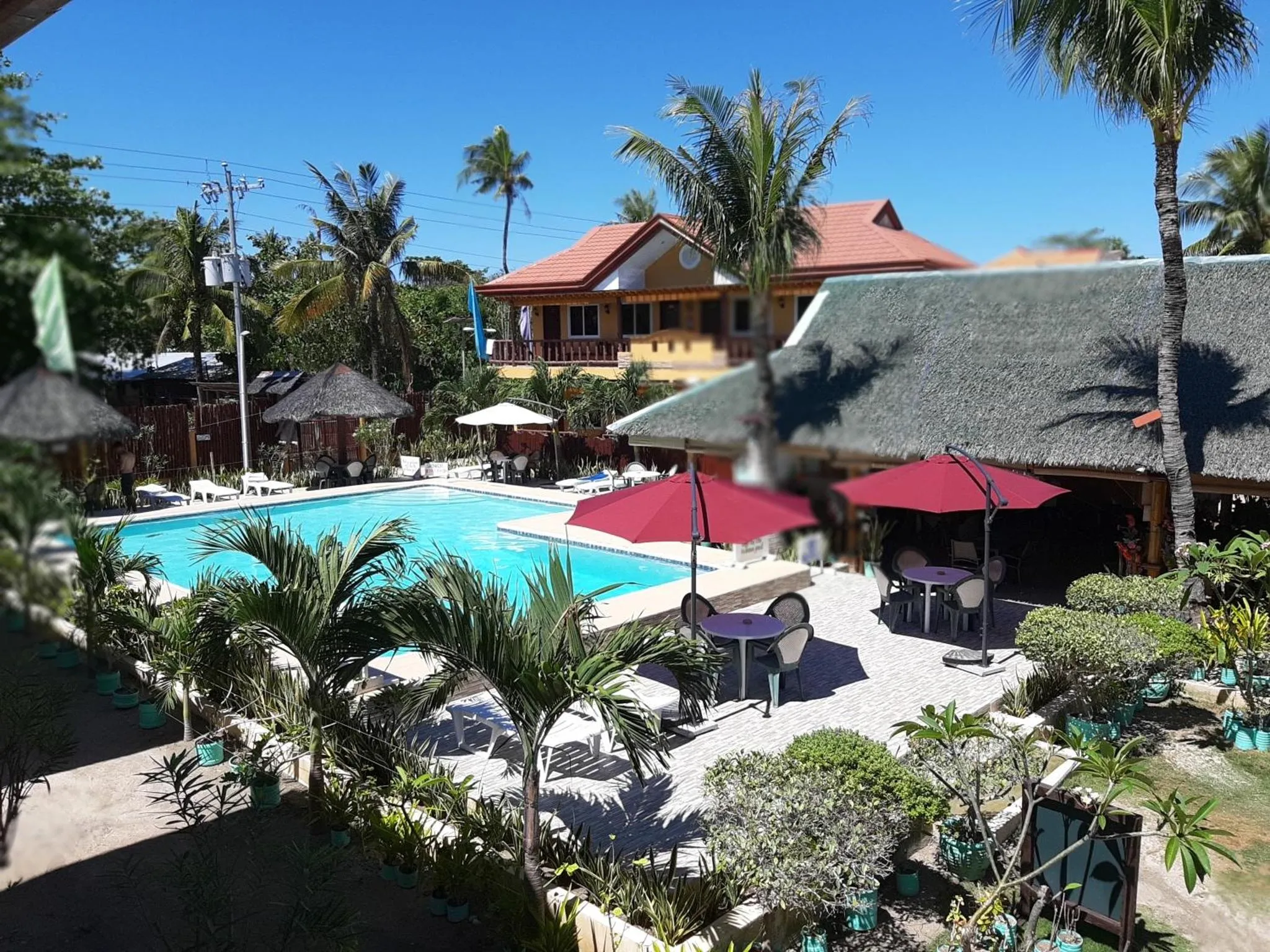 Une piscine bordée de transats et de parasols, devant un bâtiment aux toits rouges.