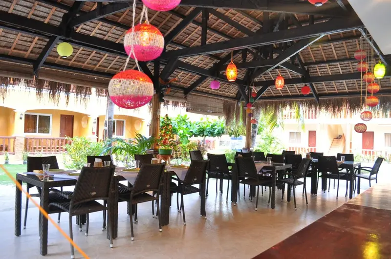 Une salle à manger extérieure avec des tables et des chaises sous un toit de chaume décoré de lanternes colorées.