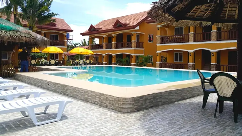 Une piscine rectangulaire bordée de chaises longues devant un bâtiment jaune à deux étages.
