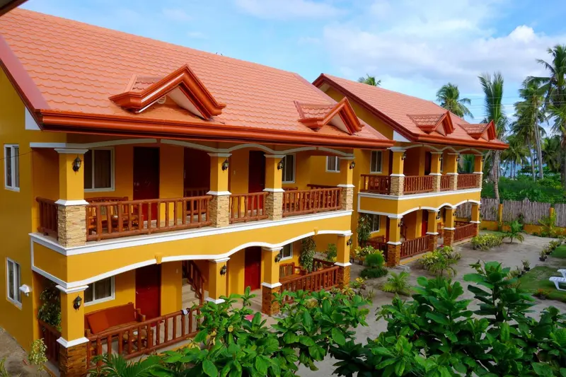 Bâtiment jaune à deux étages avec des balcons et une végétation tropicale.