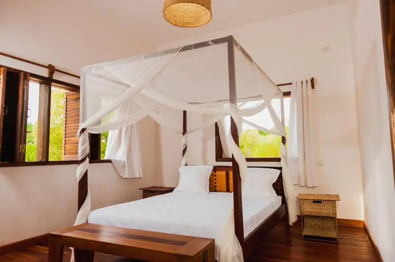 Une chambre lumineuse avec un lit à baldaquin et une vue sur la végétation.