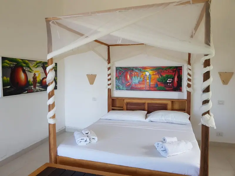 Un lit à baldaquin blanc se trouve dans une chambre décorée de tableaux colorés.