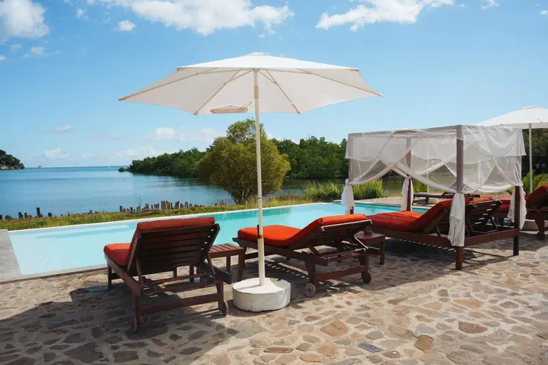 Transats et parasols bordent une piscine turquoise avec vue sur la mer.