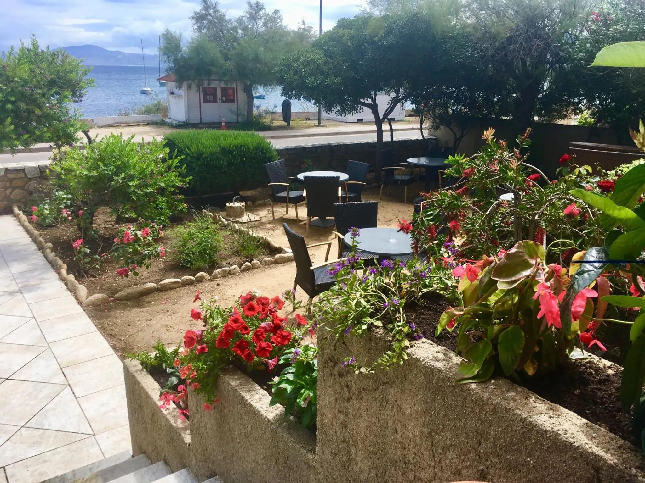 Jardin fleuri avec mobilier de terrasse et vue sur la mer.