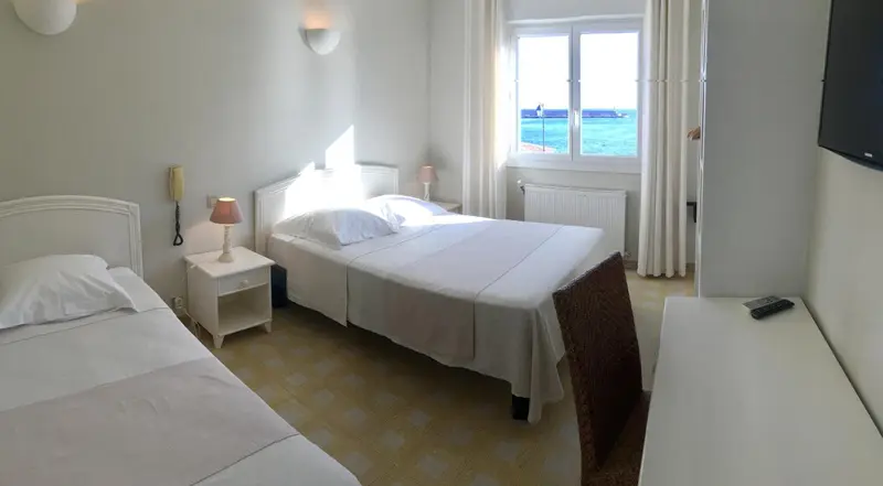 Une chambre lumineuse avec deux lits simples et une vue sur la mer par la fenêtre.