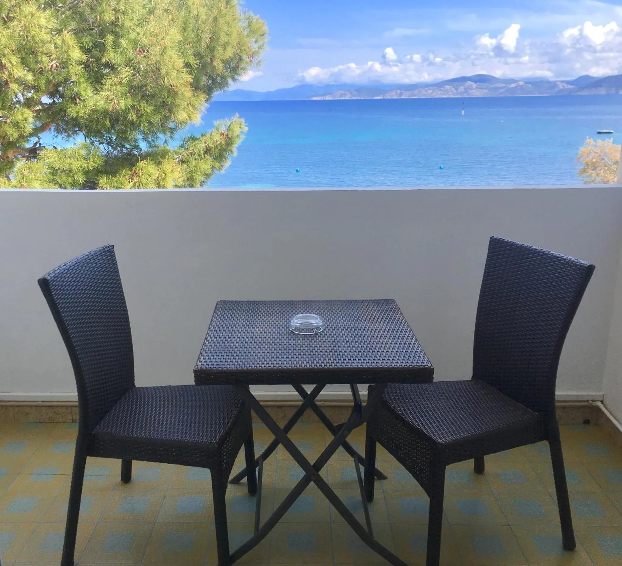 Une table et deux chaises en osier sur une terrasse ensoleillée avec vue sur la mer.