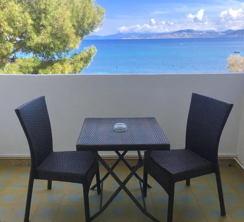 Une table et deux chaises en osier sur une terrasse ensoleillée avec vue sur la mer.