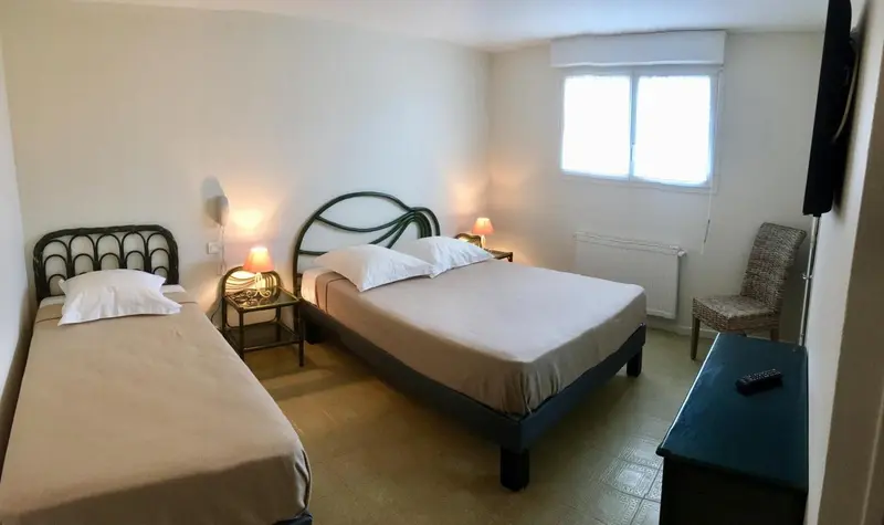 Une chambre lumineuse avec deux lits simples et un lit double.