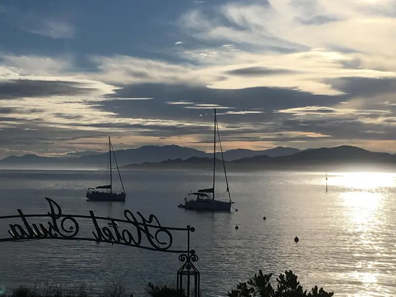 Vue sur la mer avec des voiliers au coucher du soleil.