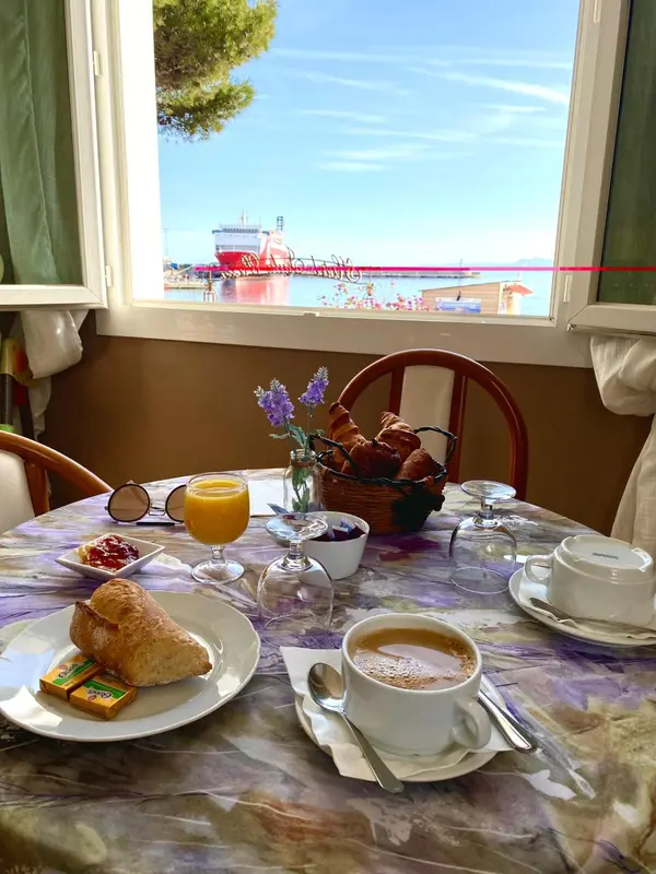 Une table est dressée avec un petit-déjeuner face à une vue sur la mer et un port.