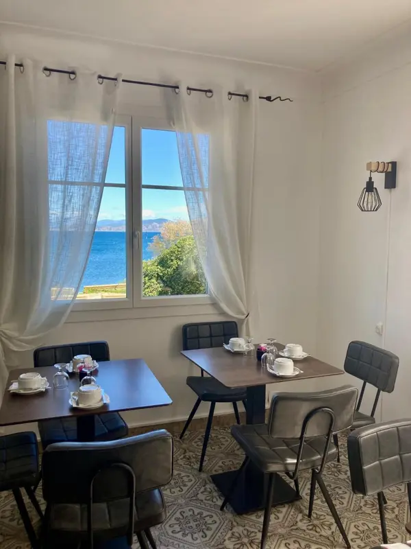 Une table est mise avec des tasses et des assiettes devant une fenêtre donnant sur la mer.