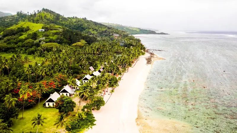 Vue aérienne d'une plage bordée de végétation luxuriante et de bungalows.