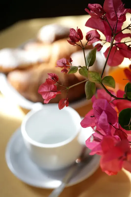 Une table accueillant une tasse de café, des viennoiseries et des fleurs colorées.