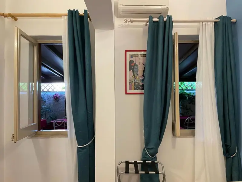 Une chambre lumineuse avec deux fenêtres et des rideaux turquoise.