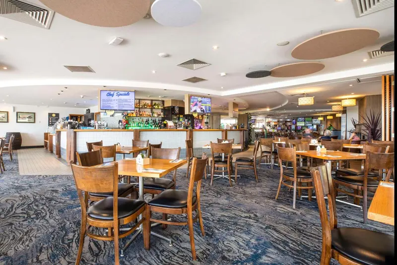 Une salle lumineuse avec un long comptoir de bar et des tables disposées sur un tapis bleu.