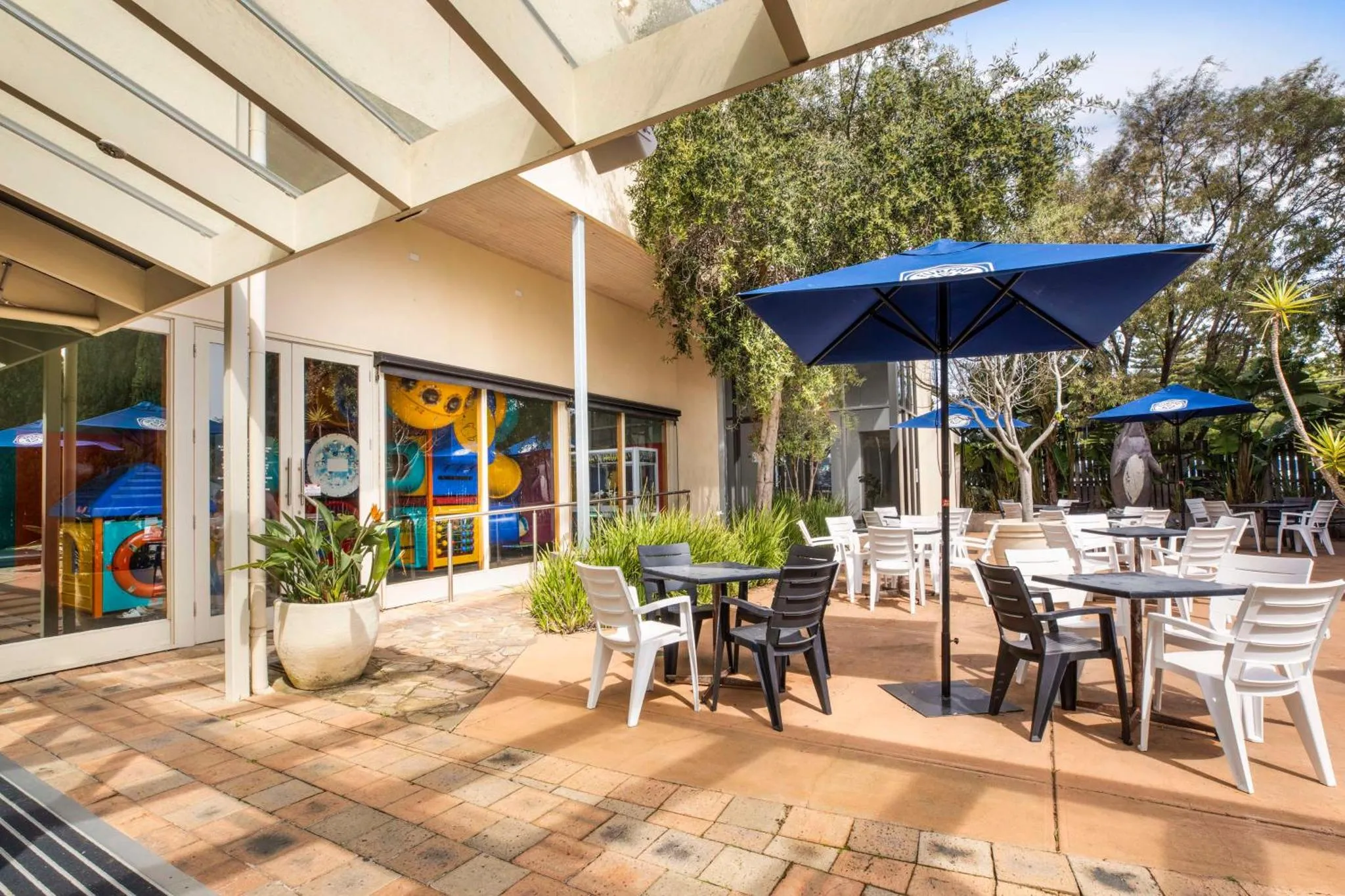 Terrasse ombragée avec tables et chaises près d'une piscine.