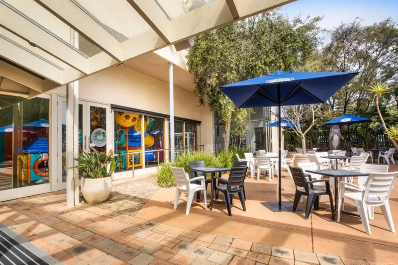 Terrasse ombragée avec tables et chaises près d'une piscine.