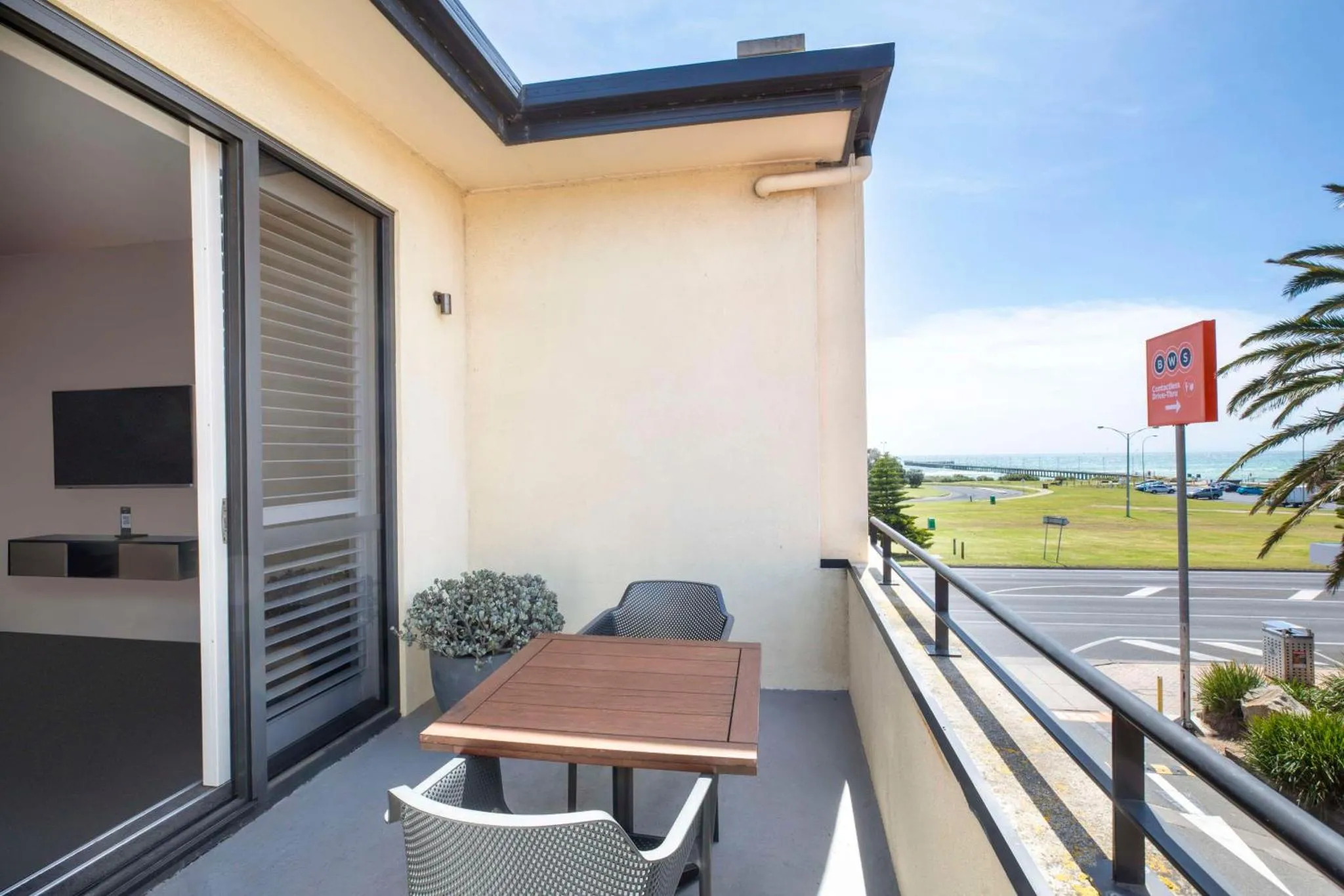 Une terrasse aménagée avec table et chaises offre une vue sur la mer et un espace vert.