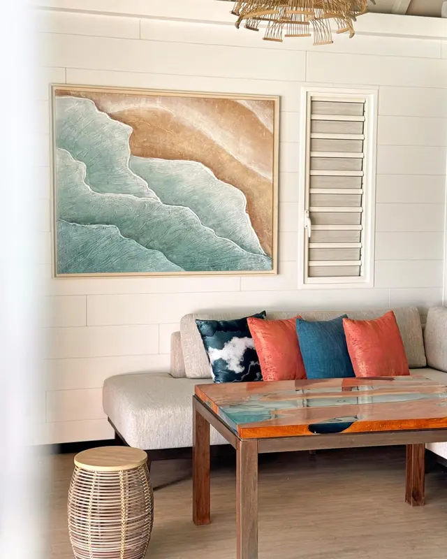 Un canapé gris et des coussins colorés se trouvent devant une grande peinture abstraite représentant des vagues.