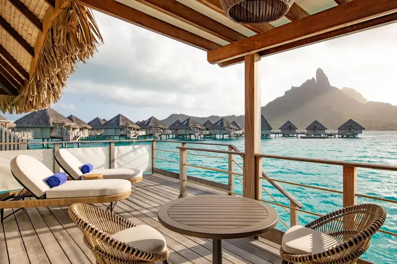 Terrasse en bois avec mobilier d'extérieur donnant sur une eau turquoise et des montagnes.