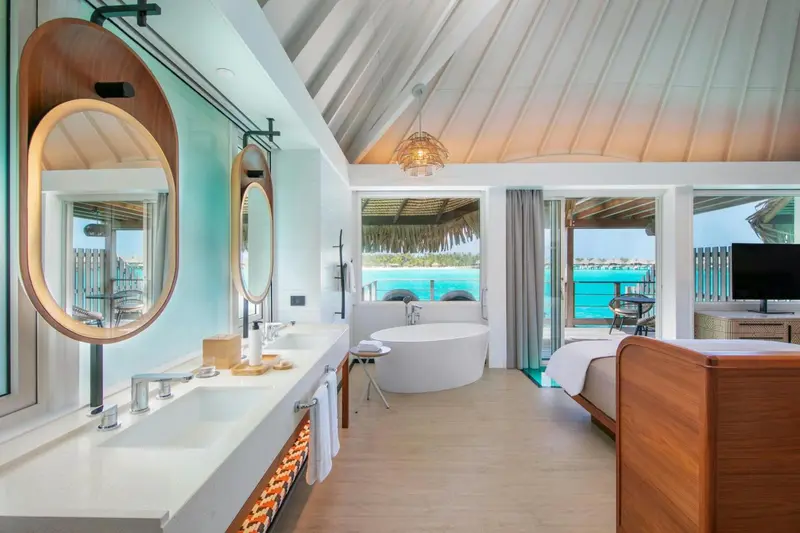 Une salle de bain lumineuse avec baignoire et vasque ouverte sur une chambre.