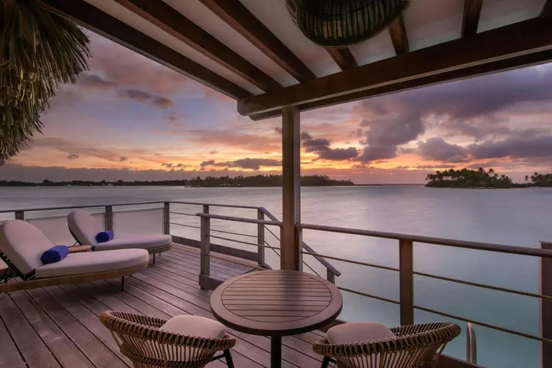 Terrasse en bois avec mobilier d'extérieur donnant sur une mer calme au coucher du soleil.