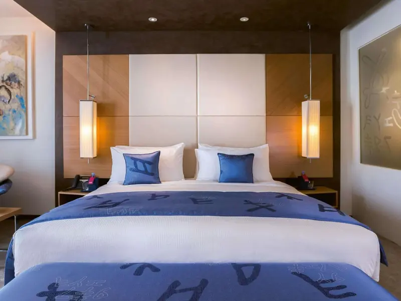 Une chambre lumineuse avec un grand lit recouvert d'une couette blanche et de coussins bleus.
