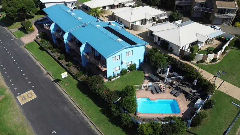 Vue aérienne d'un bâtiment bleu avec une piscine et un jardin verdoyant.