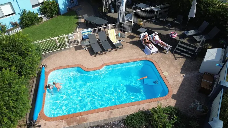 Vue aérienne d'une piscine avec des transats et des personnes se relaxant au soleil.