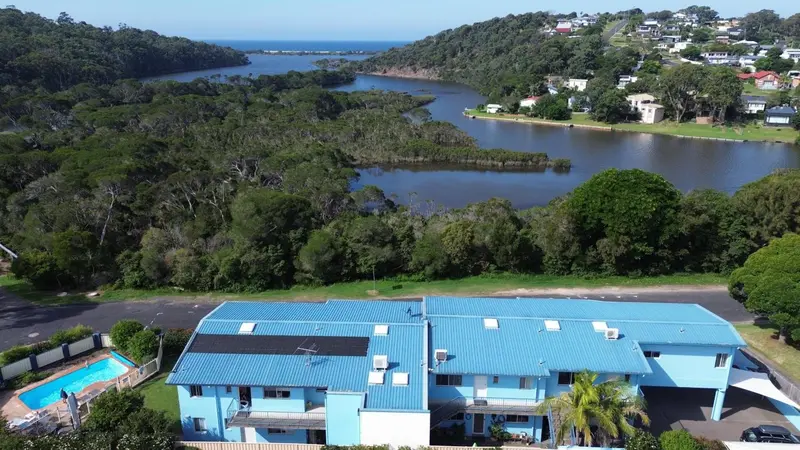 Vue aérienne d'un complexe hôtelier bleu et blanc au bord d'une rivière côtière.