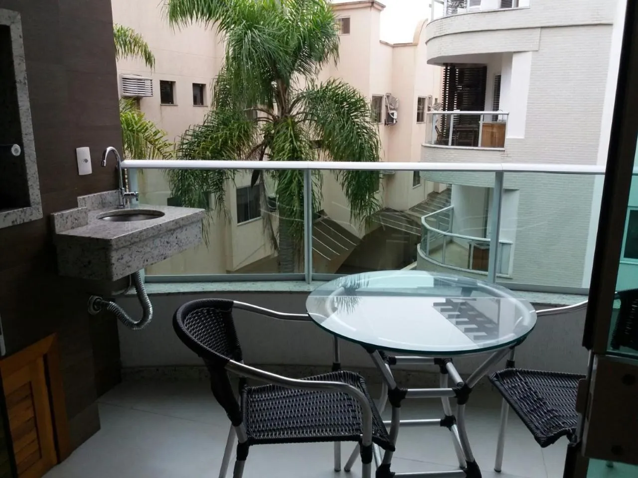 Une petite terrasse avec un évier et une table ronde en verre.