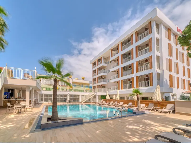 Bâtiment blanc à plusieurs étages avec des balcons et une piscine en contrebas.