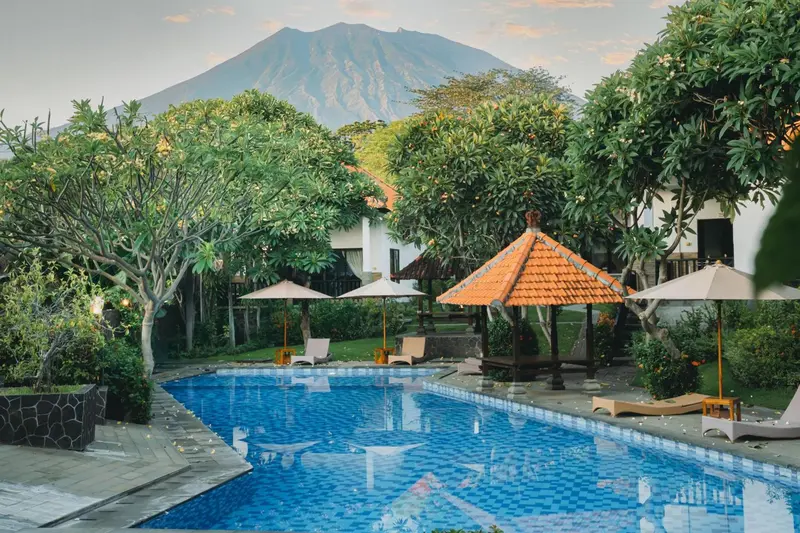 Une piscine rectangulaire bordée de chaises longues, avec une végétation luxuriante et une montagne en arrière-plan.