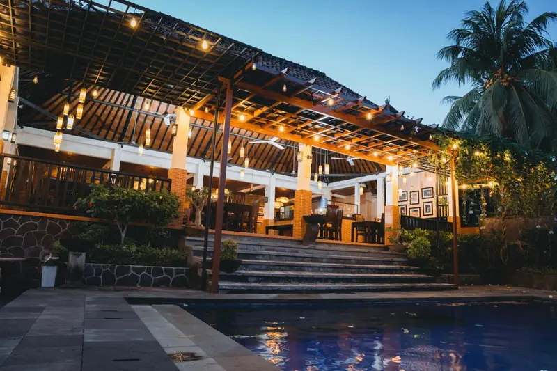 Terrasse illuminée avec piscine au premier plan et végétation tropicale.