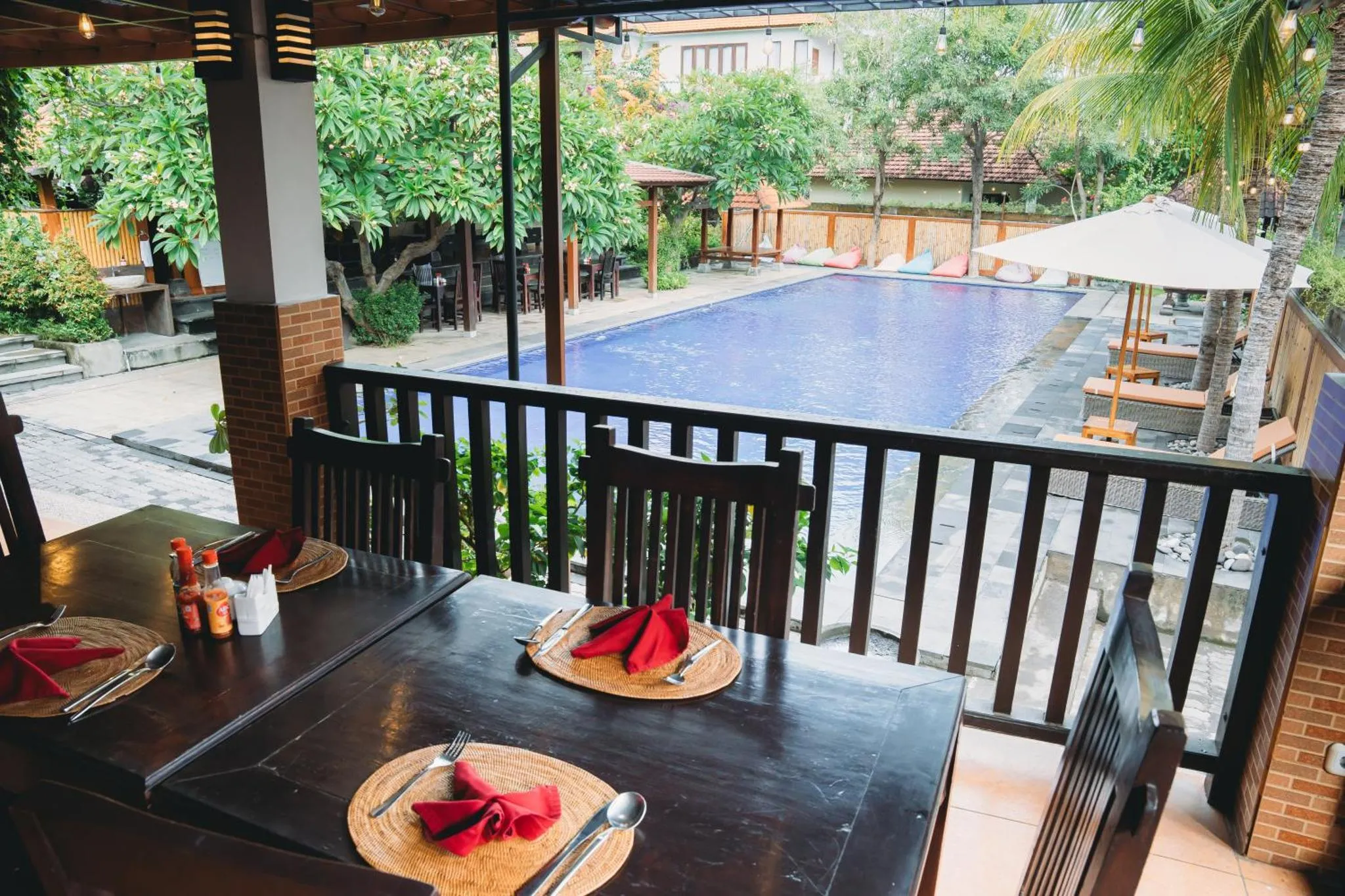 Une table est dressée sur une terrasse ombragée, face à une piscine.