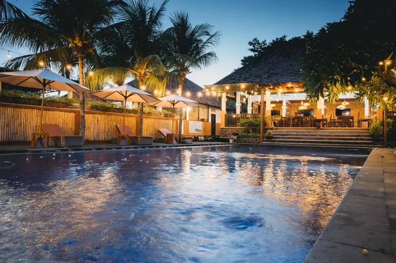 Terrasse avec piscine et végétation tropicale illuminée.