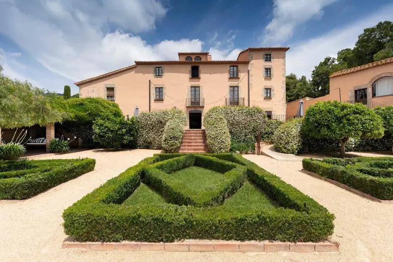 Bâtiment de couleur claire avec un jardin soigné et des parterres de buis.