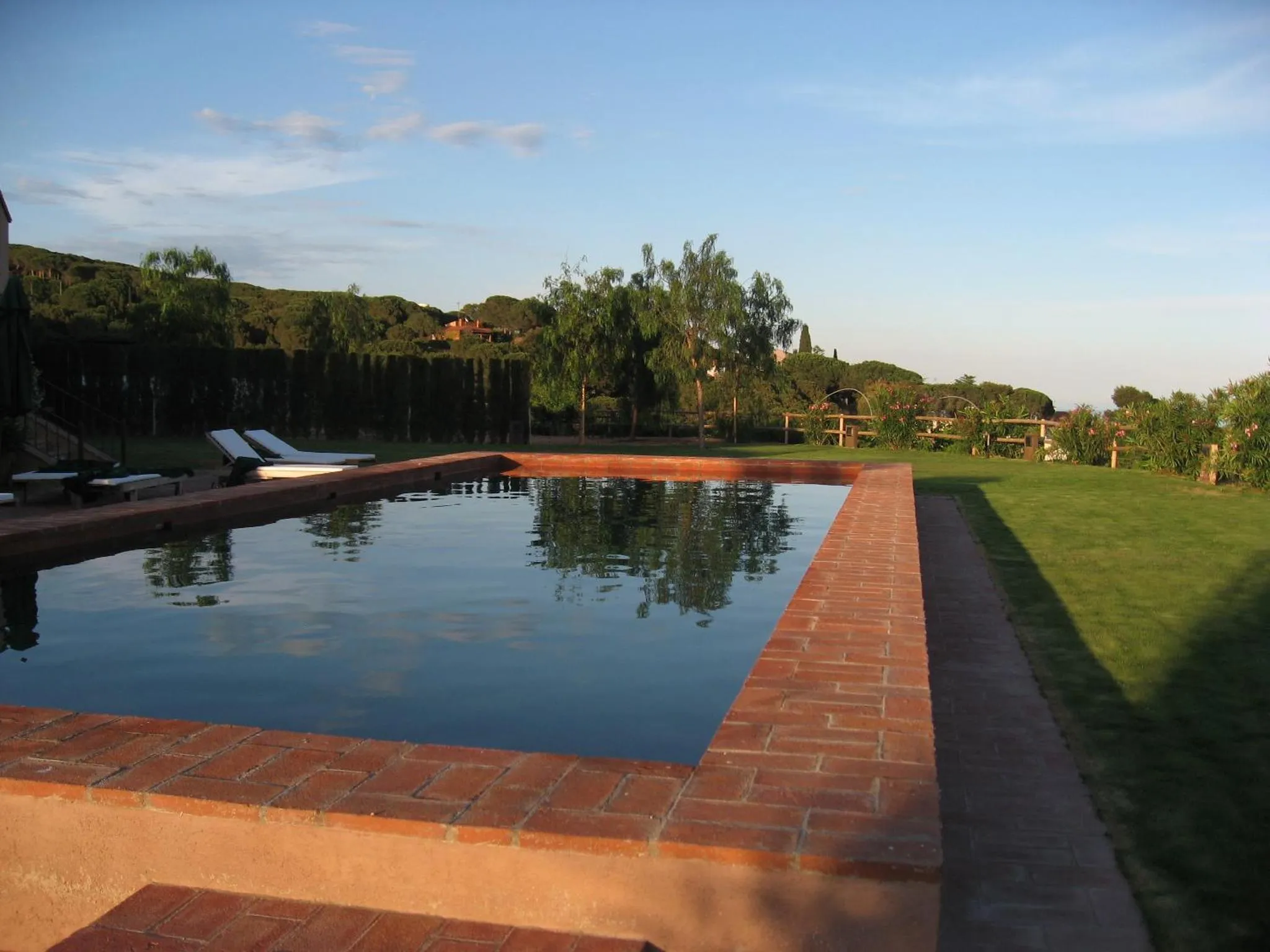Une piscine rectangulaire bordée de briques, avec des transats et une végétation luxuriante en arrière-plan.